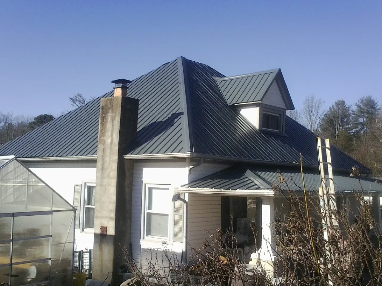 Dark blue standing seam metal roof on a white farmhouse with dormer — Slate & Tile Roof Repair by Roofing Brothers in Ames