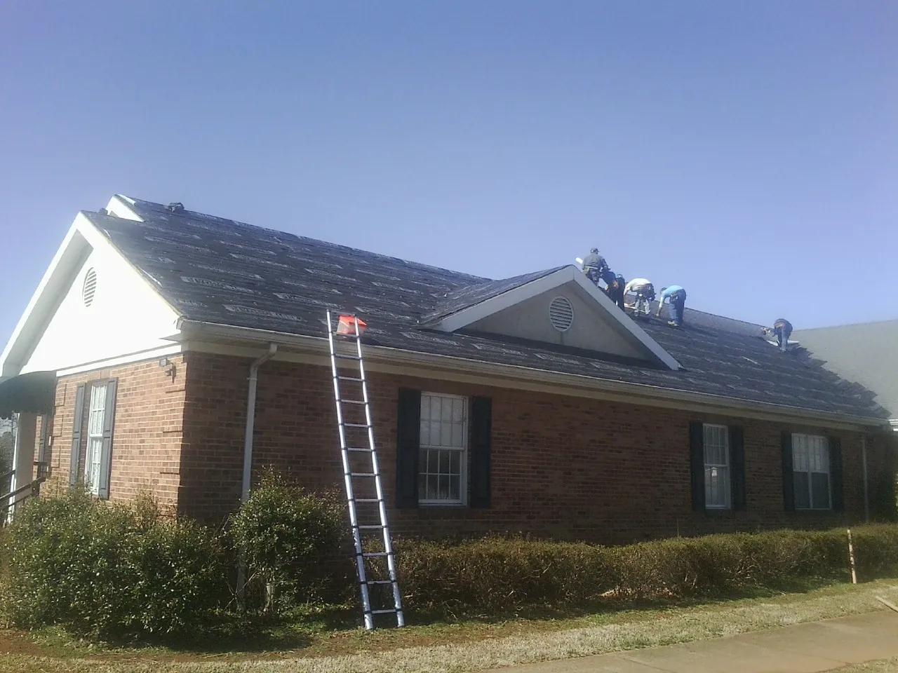 Crew tearing shingles off a brick ranch roof with a ladder set — Metal Roof Repair work by our crew in Ames
