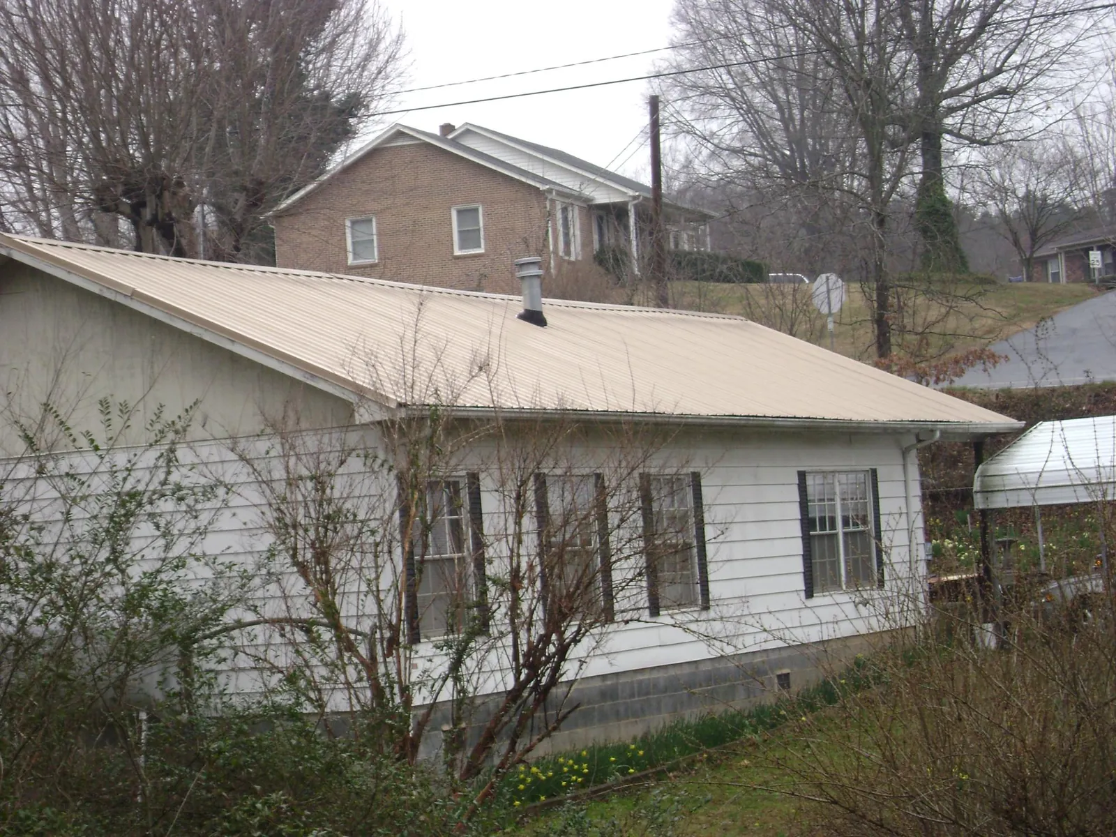 Tan metal roof on a white sided house set into a hillside — Commercial Roofing by Roofing Brothers in Ames