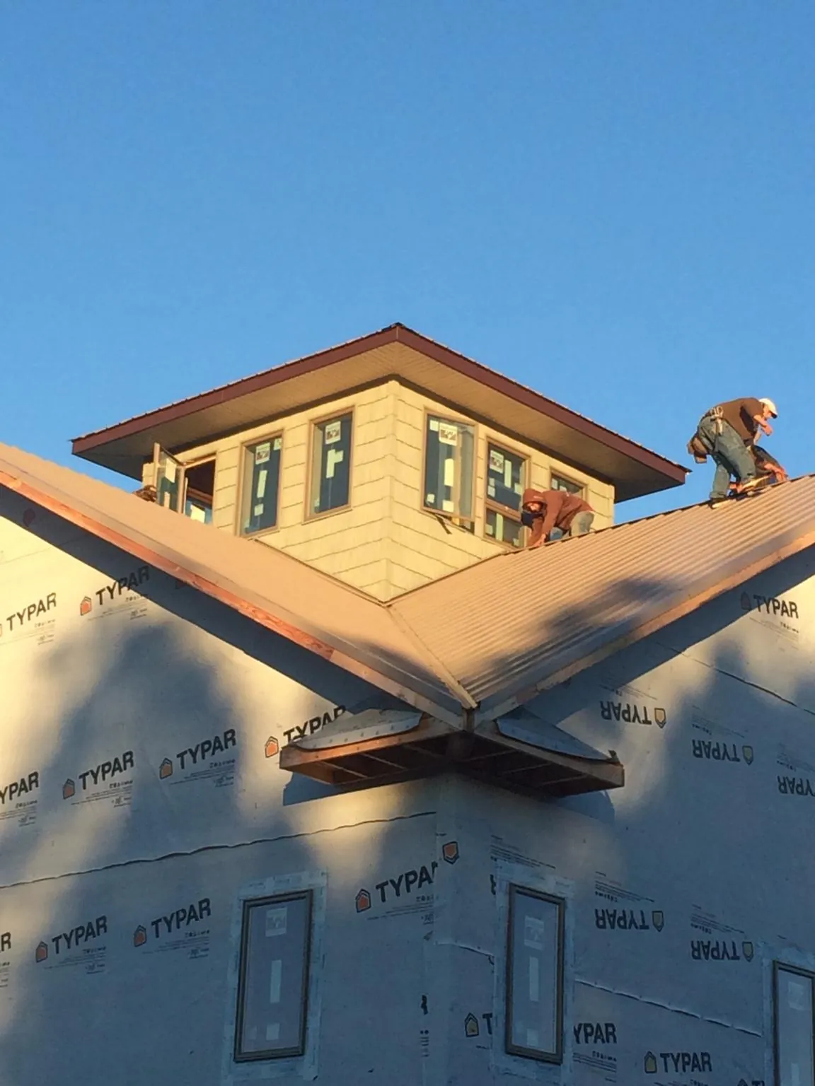 Roofers working around a rooftop cupola on a new metal roof at sunset — Roof Waterproofing in Ames by Roofing Brothers